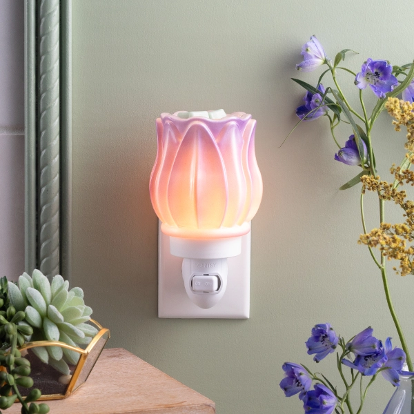 Scentsy Prismatic Petals Mini Wax Warmer plugged into a wall outlet, featuring a glowing iridescent glass shade shaped like a blooming flower.