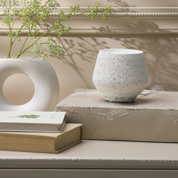 A Scentsy Air - Bespeckled sits on a platform near books and a vase with greenery.