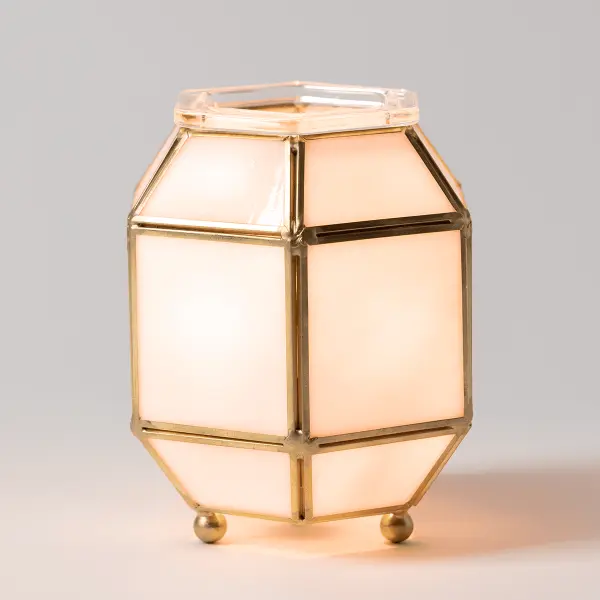 The Scentsy Clara Flameless Warmer glowing with warm light through marbled glass panels and brass framing.