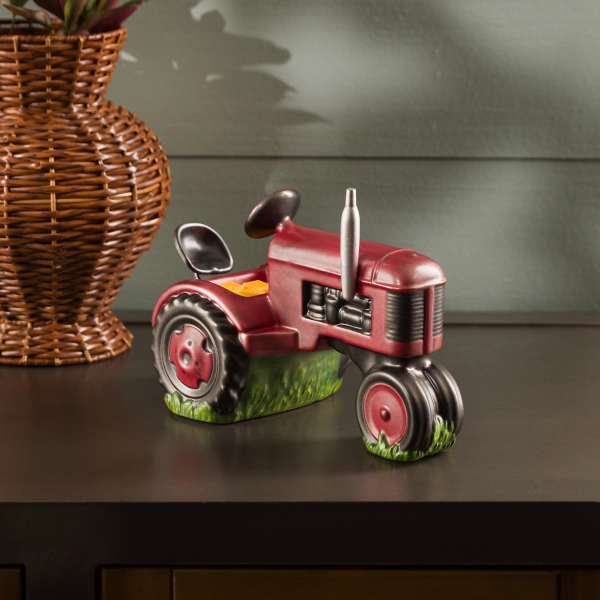 he Scentsy Country Roots Wax Warmer featuring a hand-painted, antique red ceramic tractor sitting on a patch of green grass.