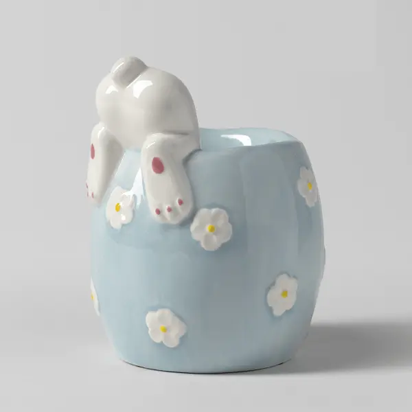 The Scentsy Curious Cottontail Tart Warmer featuring a white bunny digging into a pastel blue ceramic pot decorated with painted white daisies.