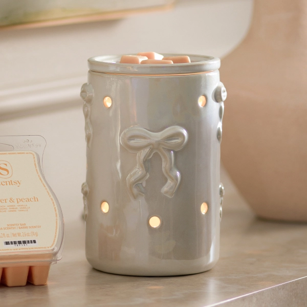 The Scentsy Dreamers Bow Candle Warmer in a pearlized white ceramic finish featuring a dainty sculpted bow and glowing vent holes.