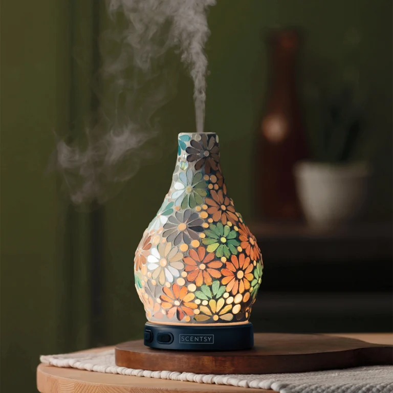 The Scentsy Enrich Diffuser glowing with hand-cut floral mosaic tiles on a wooden table, releasing a cool mist.