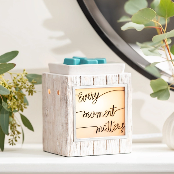 The Scentsy Every Moment Matters Candle Warmer in a white faux-wood ceramic finish featuring a glowing window with wire lettering.