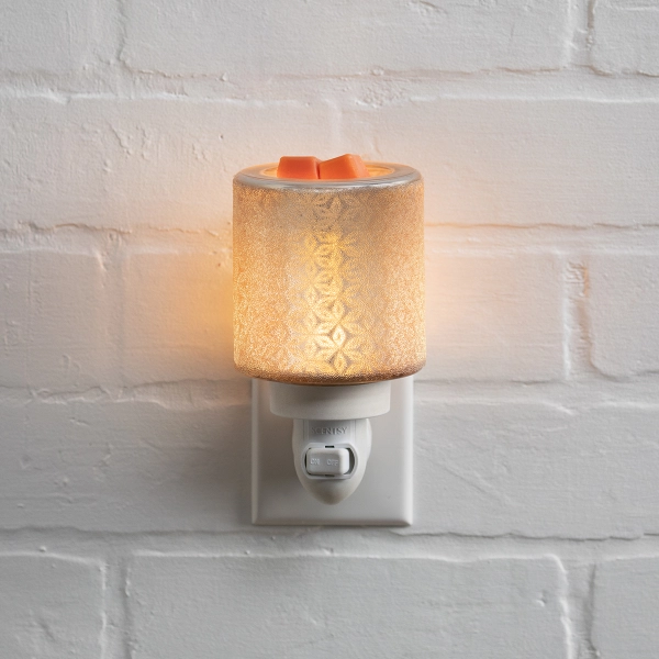 The Scentsy Fancy Filigree Mini Wax Warmer glowing warmly with an elegant laser-cut floral pattern coated in sparkling glass beads.