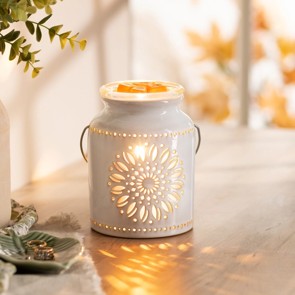 The Scentsy Heirloom Flower Candle Warmer in white ceramic with a glowing laser-cut sunflower and rustic wire handle.