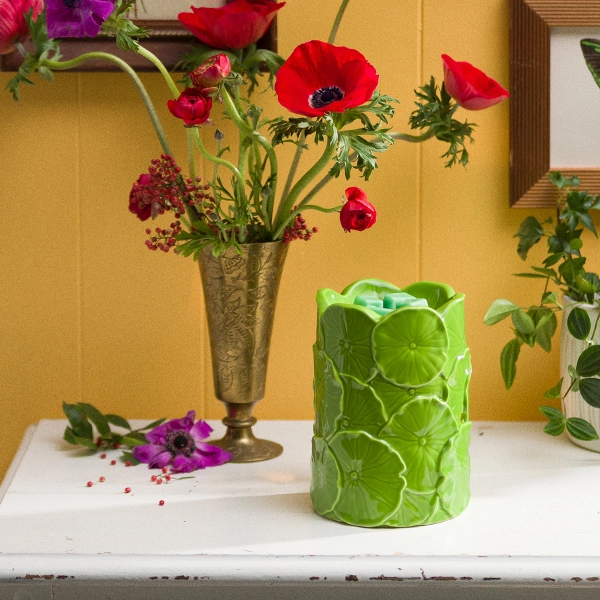 The Scentsy Leap & Lily Tart Warmer is a bright green ceramic cylinder covered in sculpted, dimensional lily pads next to red flowers.