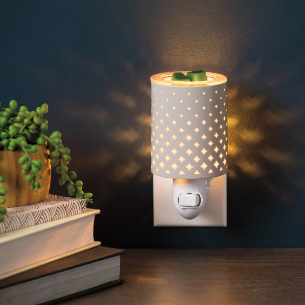 The Scentsy Light From Within Mini Electric Fragrance Melter is a white metal wall plug featuring small diamond cutouts that cast a glowing star pattern.