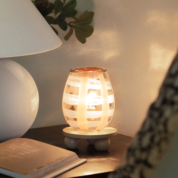 Scentsy Lightweave Wax Warmer glowing softly on a wooden base with an exposed bulb casting shadows on a nearby wall.