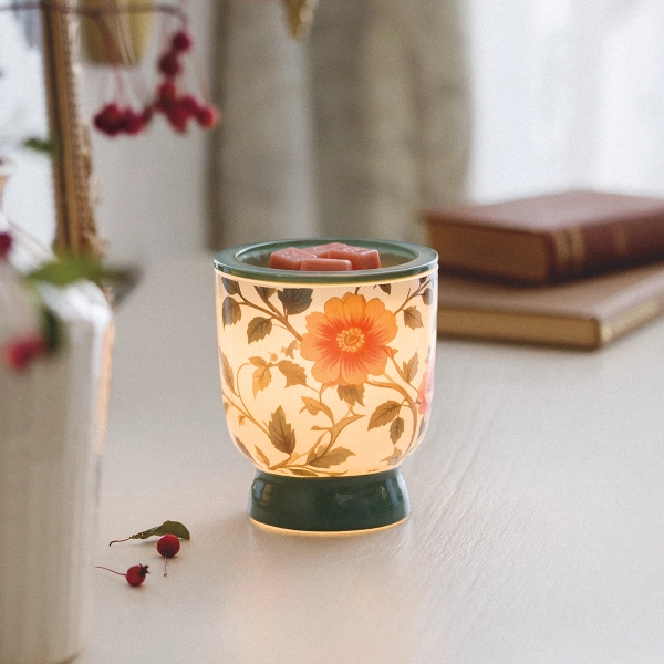 Scentsy Petal & Vine Wax Warmer glowing softly, featuring a vintage glass body adorned with peach floral patterns and elegant green leaves.
