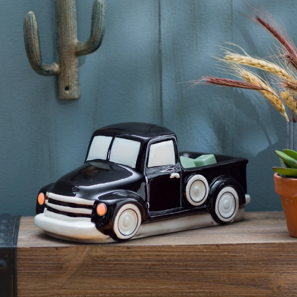 Scentsy Retro Black Truck Wax Warmer featuring a glossy black ceramic finish, white windows, and classic whitewall tires sitting on a wooden shelf.