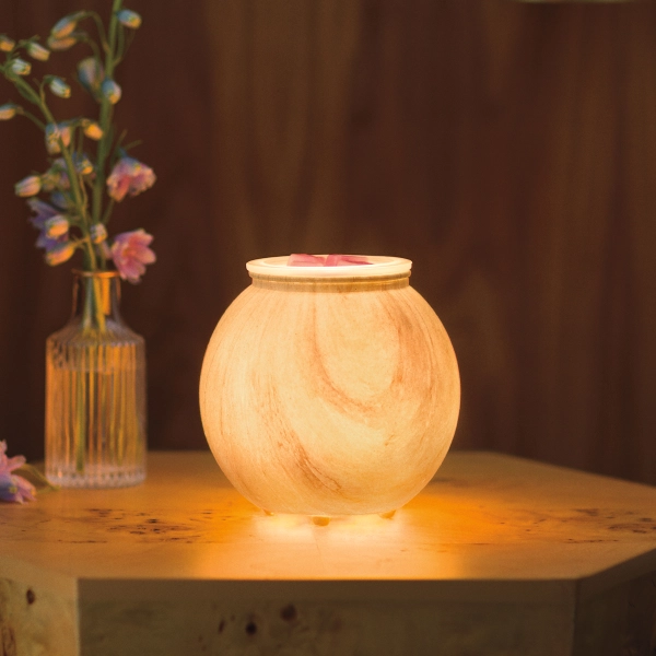 Scentsy Sanded Linea Wax Warmer featuring a frosted, glowing spherical glass body that resembles warm natural stone on a wooden table.