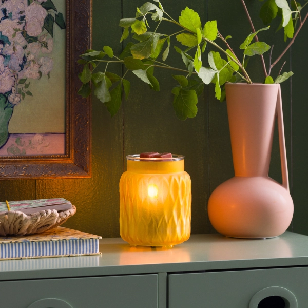 Scentsy Soft Honey Wax Warmer glowing on a green cabinet, featuring frosted golden glass with a geometric vintage texture.