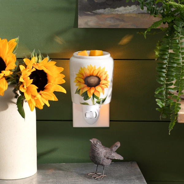 Scentsy Sunflower Mini Wax Warmer plugged into a green wall, featuring a hand-painted yellow sunflower on rustic white ceramic.