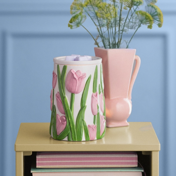 Scentsy Tulip Meadow Wax Warmer resting on a table, featuring a white ceramic body with hand-painted, embossed pink tulips and vibrant green leaves.