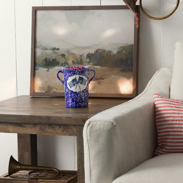 Speckled blue and white Scentsy Old Glory Wax Warmer with a red dish and crossed flags, sitting on a rustic wooden table.